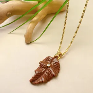 Vue détaillée du collier chaîne doré avec pendentif feuille en pierre de soleil marron.