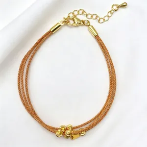 Primo piano del bracciale in maglia dorata multistrato con perline delicate e chiusura.