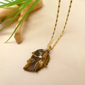 Détail de collier pendentif feuille sculptée en cristal naturel artisanal avec chaîne en or.