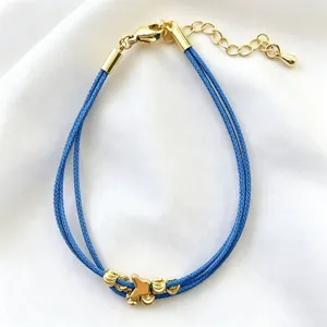 Primo piano di un bracciale in corda blu fatto a mano con perle dorate su raso bianco.