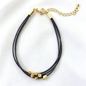 Primo piano dettagliato di un bracciale multistrato in corda nera con perline dorate.