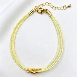 Vista dettagliata del bracciale in corda intrecciata gialla a più strati con perle dorate.