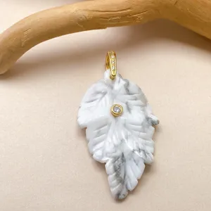 Pendentif feuille en cristal blanc sculpté à la main avec bélière dorée et pierre centrale.