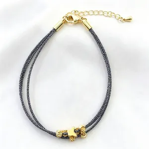 Vista dettagliata del bracciale intrecciato multistrato nero e bianco con ciondolo a farfalla dorata.