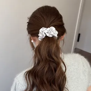 Detail view of a shimmering silver satin hair scrunchie with rhinestones, worn gracefully.
