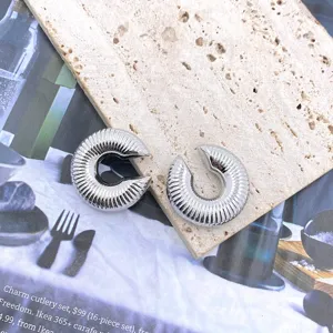 Close-up of silver ribbed C-shaped earrings, showing fine texture and modern geometric details.