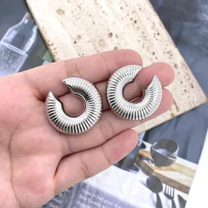 Detailed shot of chunky textured C-shaped silver earrings held in hand with stone background.
