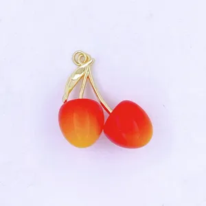 Close up of a cute red and yellow gradient cherry pendant with gold stem and leaf for DIY jewelry.
