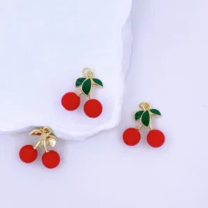 Detail view of DIY 3D cherry charms with red berries and green enamel leaves for jewelry making.