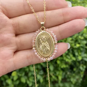 Vue détaillée du collier pendentif en cuivre plaqué or avec perles roses en main.