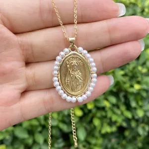 Collier doré exquis avec un pendentif ovale religioso entouré de petites perles blanches.