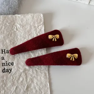 Rood fluwelen strik haarspeld detail met gouden metalen strik en zachte textuur.