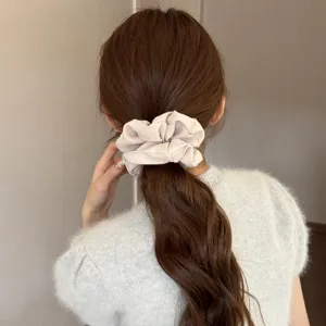 Close-up detail of a soft beige satin hair scrunchie worn on brown tied hair, elegant.