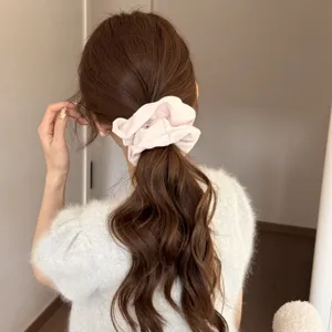 Detail shot of a soft pink satin hair scrunchie worn on wavy brown hair, elegant accessory.