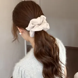 Close up view of elegant satin hair scrunchie worn on wavy brown hair, soft glossy texture detail.