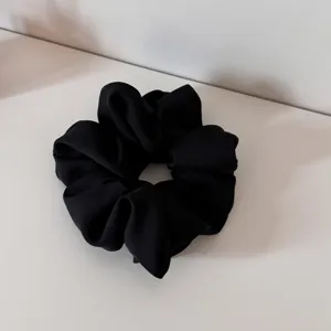 Detailed close-up of a classic black satin scrunchie, soft fabric texture and pleated design.