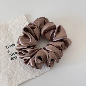 Close-up detail of a brown satin hair scrunchie decorated with sparkling rhinestones for women.