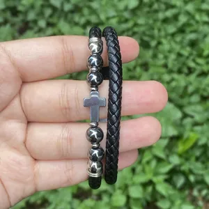 Detailansicht eines mehrschichtigen geflochtenen Lederarmbands mit Kreuz und Metallperlen.