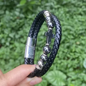 Nahaufnahme des mehrschichtigen geflochtenen Lederarmbands mit Kreuz-Anhänger und Verschluss.