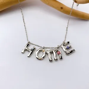 Silver metal letter necklace detail featuring HOME pendant with colorful evil eye charms.