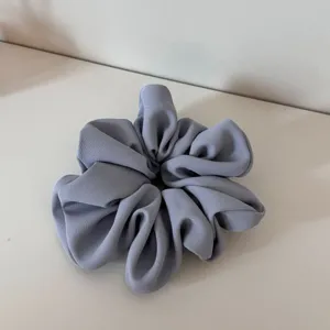 Detailed view of a light grey satin hair scrunchie, soft pleated texture for everyday wear.