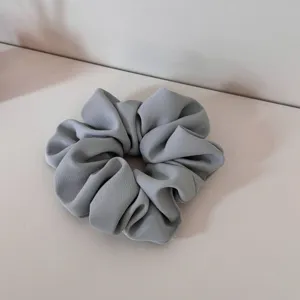 Gray fabric hair scrunchie detail shot, showcasing soft texture and gathered pleat design for everyday styling.