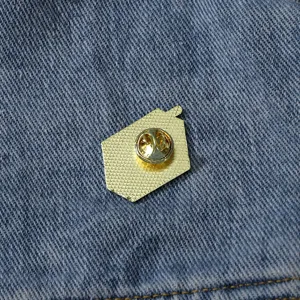 Gedetailleerd overzicht van de gouden metalen emaillen broche rug, veilige sluiting op denim.