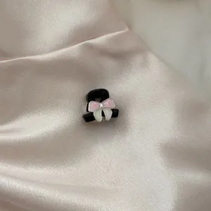 Detailed close-up of a chic black metal mini hair claw clip with a cute pink and white bow.