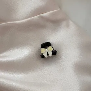 Detailed close-up of a mini black hair claw clip featuring a elegant cream white enamel bow.