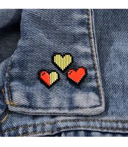 Close-up detail of cute pixel heart metal brooches pinned on stylish blue denim fabric.