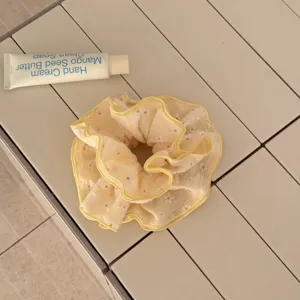 Gros-plan d'un chouchou de cheveux en tissu jaune à motif de marguerites à 4 couches.