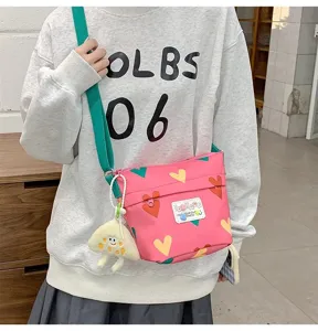 Cute pink canvas crossbody bag with heart prints, green strap, and playful charm pendant.