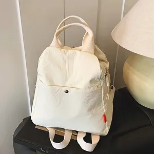 Detail shot of a minimalist beige canvas backpack, showing sturdy handles and pocket.