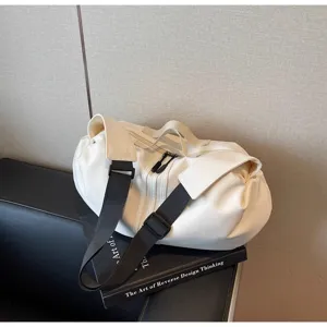 Close-up detail of a white casual travel gym bag with black strap on dark book display.