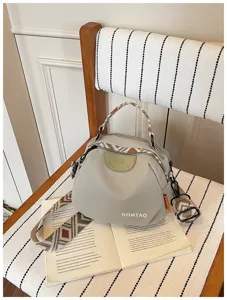 Detailansicht der hellgrauen Muscheltasche mit gemustertem Schultergurt und Frontlogo.