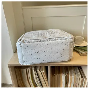 Detail shot of a white star pattern travel bag with embroidered text on a wooden shelf.