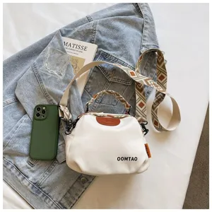 Detailansicht einer weißen Muscheltasche mit gewebtem Riemen und Jeans-Hintergrund.