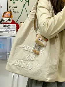 Canvas tote bag detail, casual everyday shoulder bag with cute plush charm and embroidery.