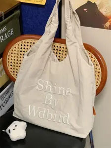 Detailed view of beige canvas tote bag with embroidered letters, casual everyday handbag.