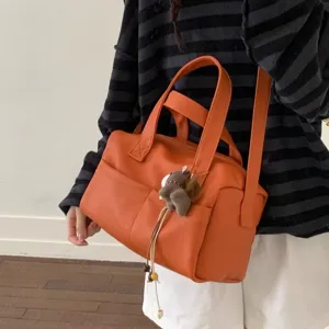 Orange PU leather handbag detail showing dual top handles, front pockets, and cute charm.