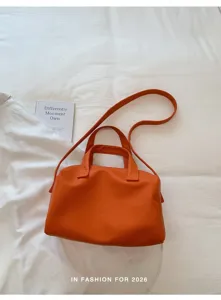 Orange leather handbag detail showing texture, dual handles and long shoulder strap for daily wear.