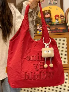 Close-up detail of casual red nylon tote bag with embroidered letters and plush keychain.