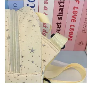 Close-up detail shot of cute yellow canvas backpack featuring silver star prints and zipper.