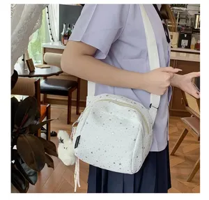 Detailed view of white star print crossbody shoulder bag with cute plush charm in cafe scene.