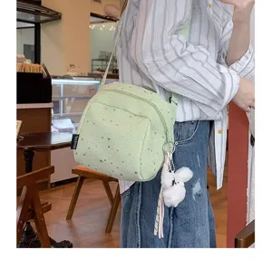 Detail shot of light green star print crossbody bag with cute plush charm in cafe setting.