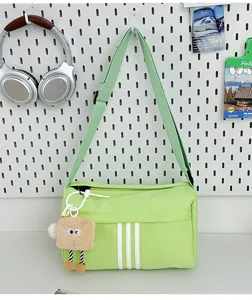 Green canvas crossbody bag detail shot showing adjustable strap, white stripes and plush charm.