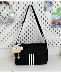 Casual canvas crossbody bag detail showing the three-stripe design and cute plush pendant.