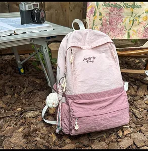 Outdoor pink contrast backpack detail showing front zipper pocket and cute hanging pendant.