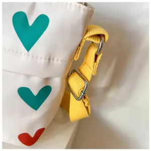 Canvas shoulder bag detail showing heart prints, yellow strap and metal buckles.