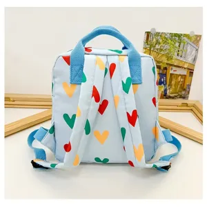 Detail view of light blue mini backpack featuring colorful heart pattern and durable blue straps.